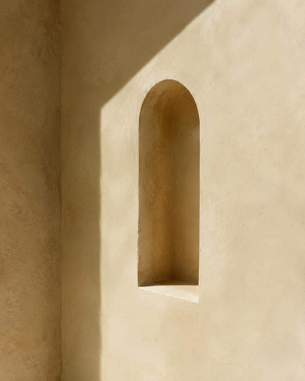 Sonnenlicht auf einer cremefarbenen Putzwand mit einer schmalen Rundbogennische